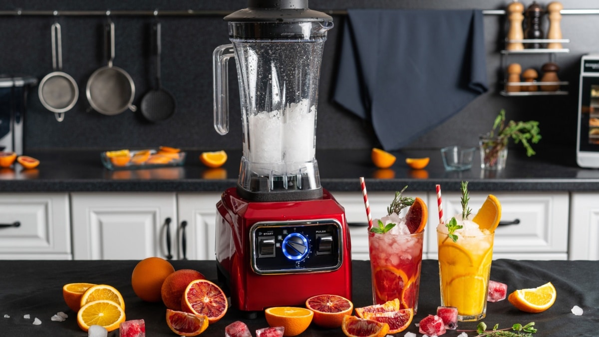 Modern electronic Red blender with crushed ice cubes and cold homemade citrus lemonade in faceted glasses with cardboard cocktail tubes.