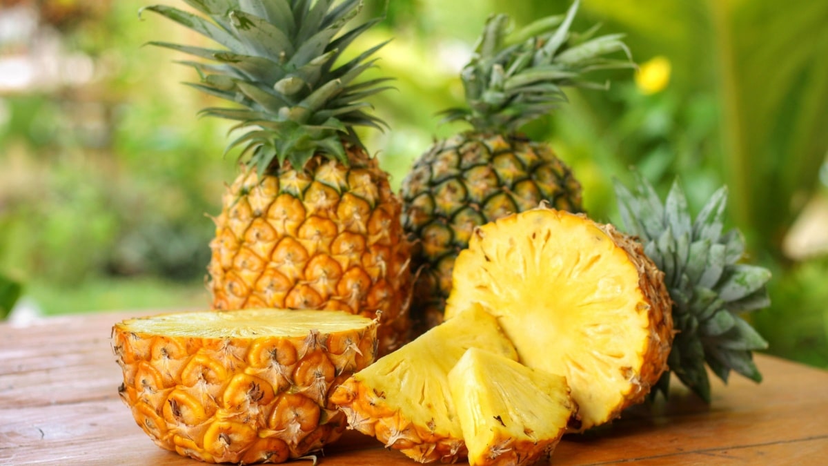 Sliced and half of Pineapple(Ananas comosus) on wooden table with blurred garden background.Sweet,sour and juicy taste.Have a lot of fiber,vitamins C and minerals.Fruits or healthcare concept.