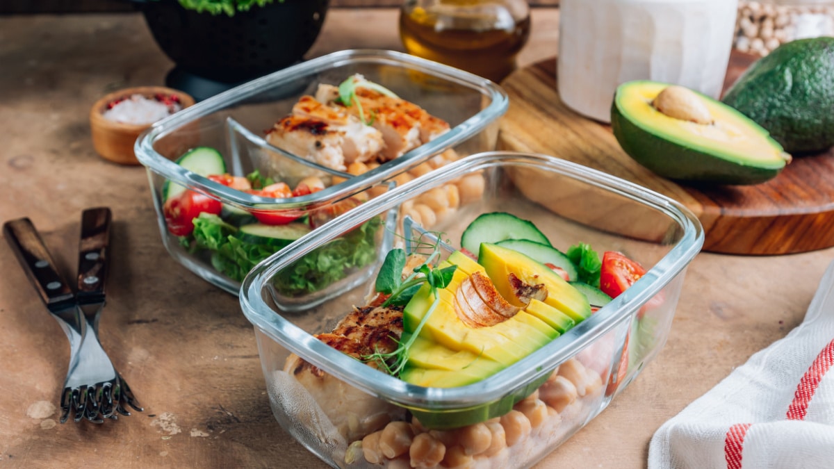 Healthy meal prep containers with chickpeas, chicken, tomatoes, cucumbers and avocados. Healthy lunch in glass containers on beige rustic background