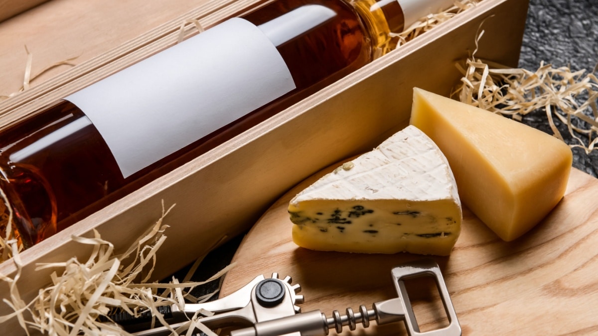 Box with bottle of wine, cheese and corkscrew on dark background