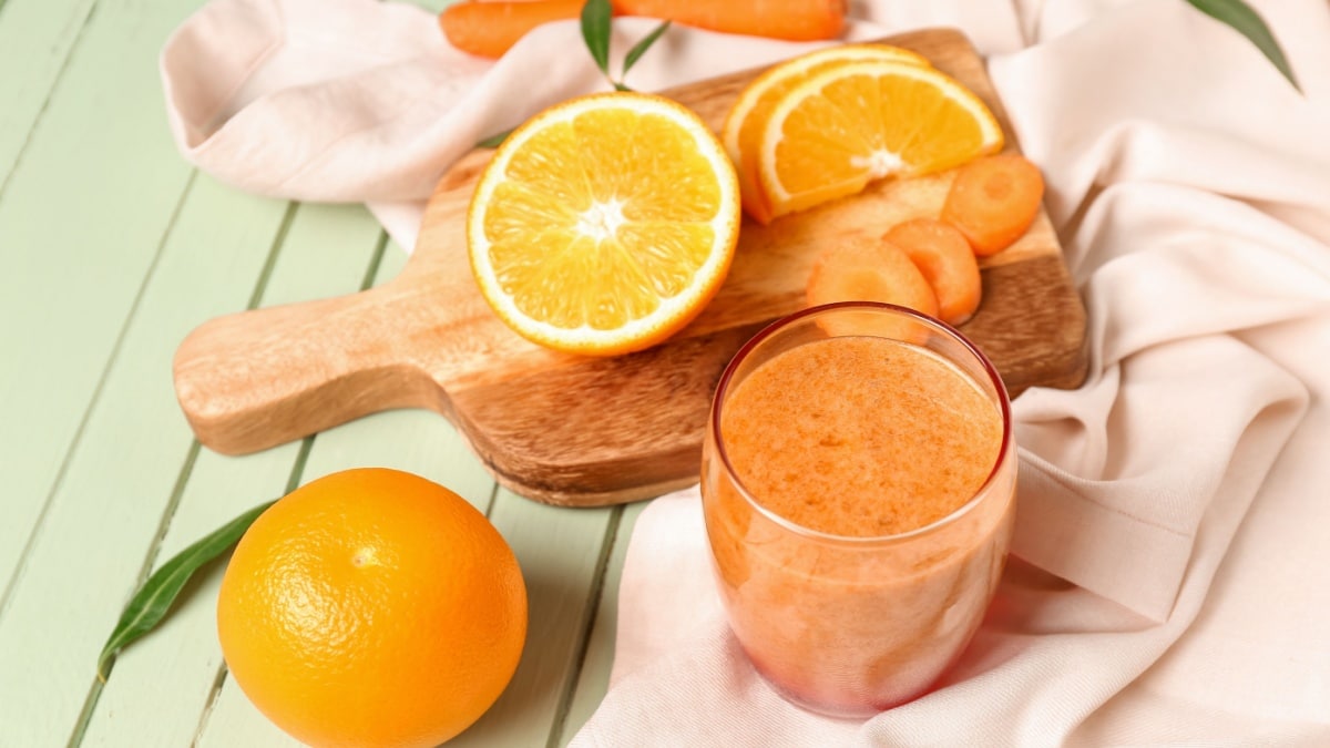 Glass of healthy orange smoothie and ingredients on green wooden table