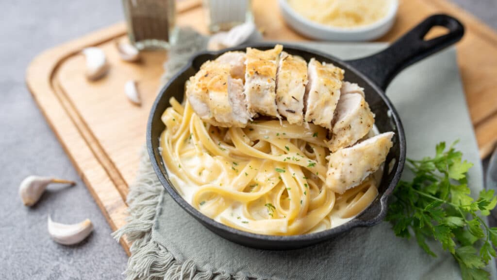 Alfredo pasta dinner with creamy white sauce with herbs and sliced chicken