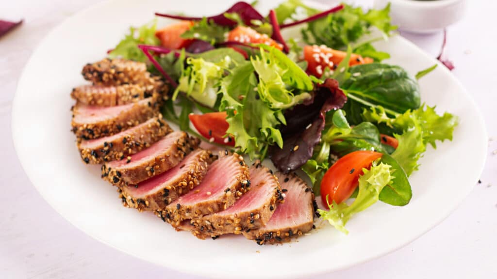Japanese traditional salad with pieces of medium-rare grilled Ahi tuna and sesame with fresh vegetable salad on a plate. Authentic Japanese food.