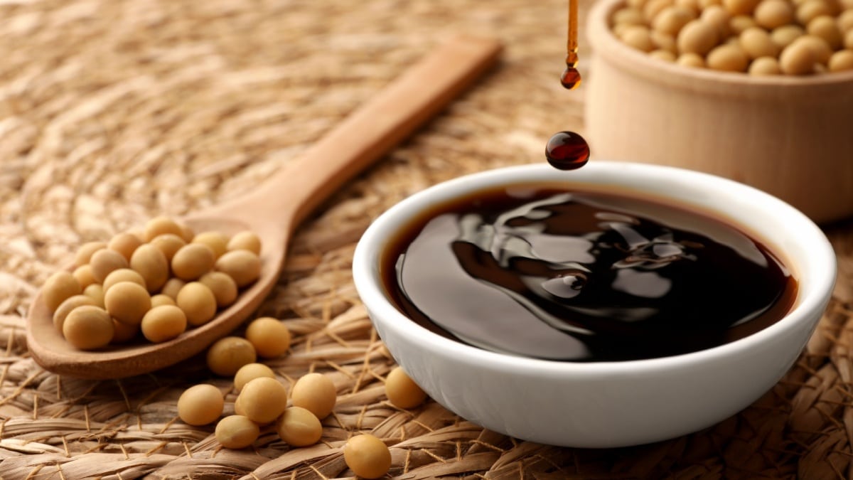 Soy sauce drops falling into bowl on wicker mat, closeup