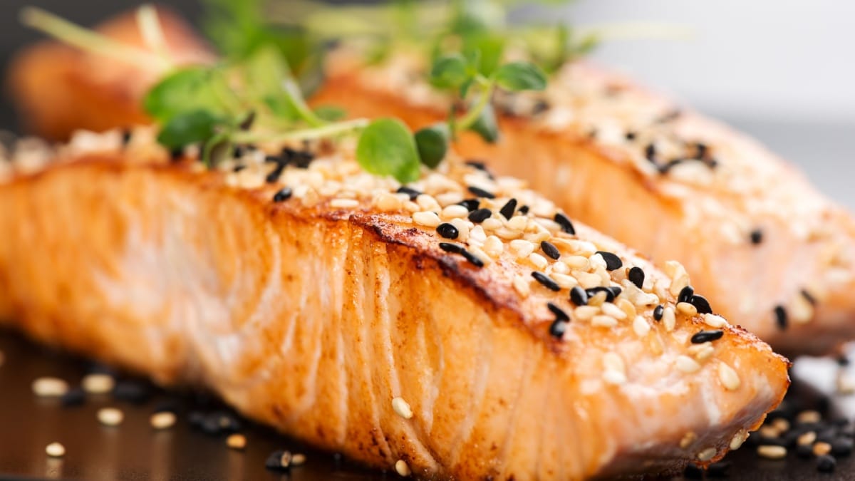 Grilled salmon, sesame seeds and marjoram on a black plate.
