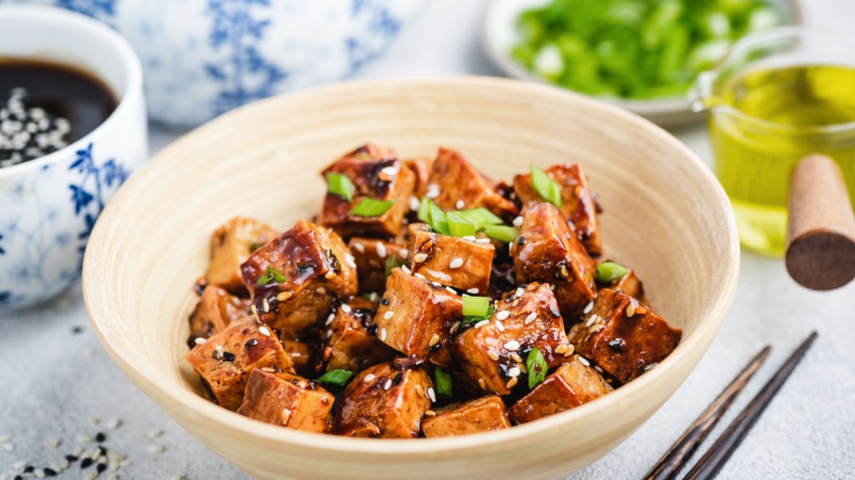 Vegan fried teriyaki tofu with scallions and sesame seeds in bamboo bowl. Asian cuisine food