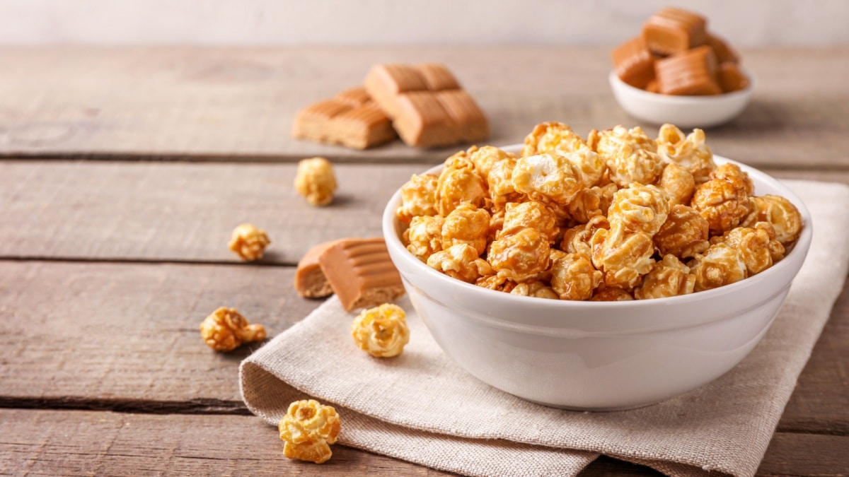 Sweet caramel popcorn and caramel candies on wooden background.